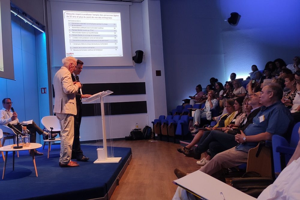 Sur scène, photo de Joachim Ertelt Bernd et Michael Scharpf, de l’Institut des sciences appliquées du conseil (Stuttgart, Allemagne), lors des Rencontres nationales des Maisons de l'information sur la formation et l'emploi (Lyon, 19 et 20 juin 2023)